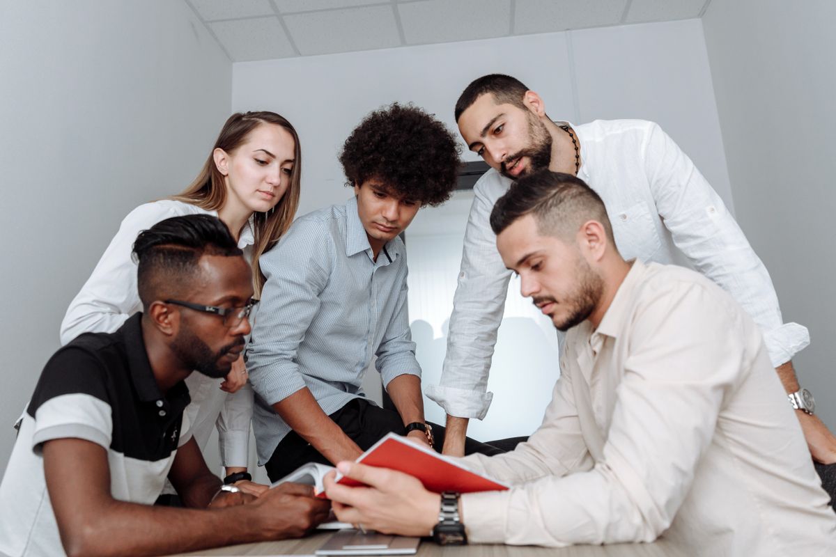 A team of five professionals gathered around a laptop, discussing work together